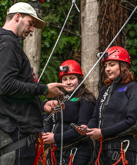 Guide instructing participants on safety gear for ziplining in Waitomo.