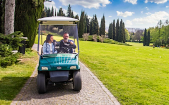 Golf cart on path at Parco Giardino Sigurtà with two people enjoying the scenic view.
