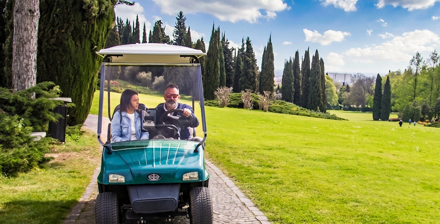 Golf cart on path at Parco Giardino Sigurtà with two people enjoying the scenic view.