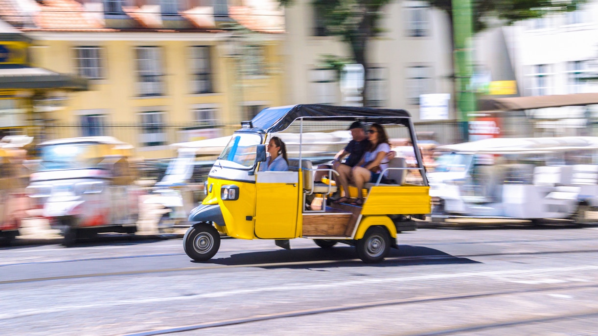 People riding a yellow tuk tuk on a street in Lisbon.