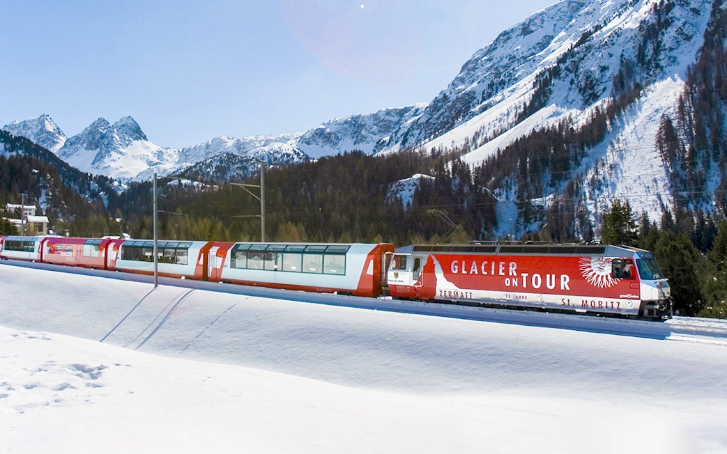 Glacier Express train traveling through snowy mountains near St. Moritz.