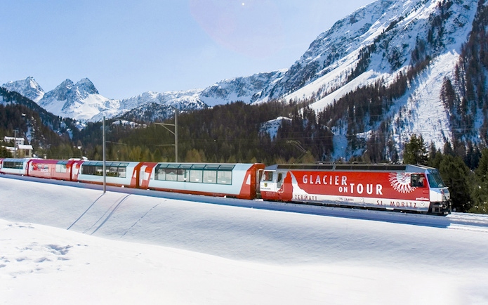 Glacier Express train traveling through snowy mountains near St. Moritz.