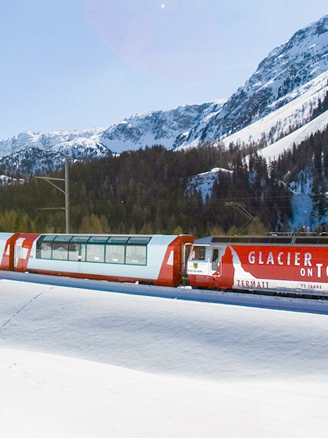 Glacier Express train traveling through snowy mountains near St. Moritz.