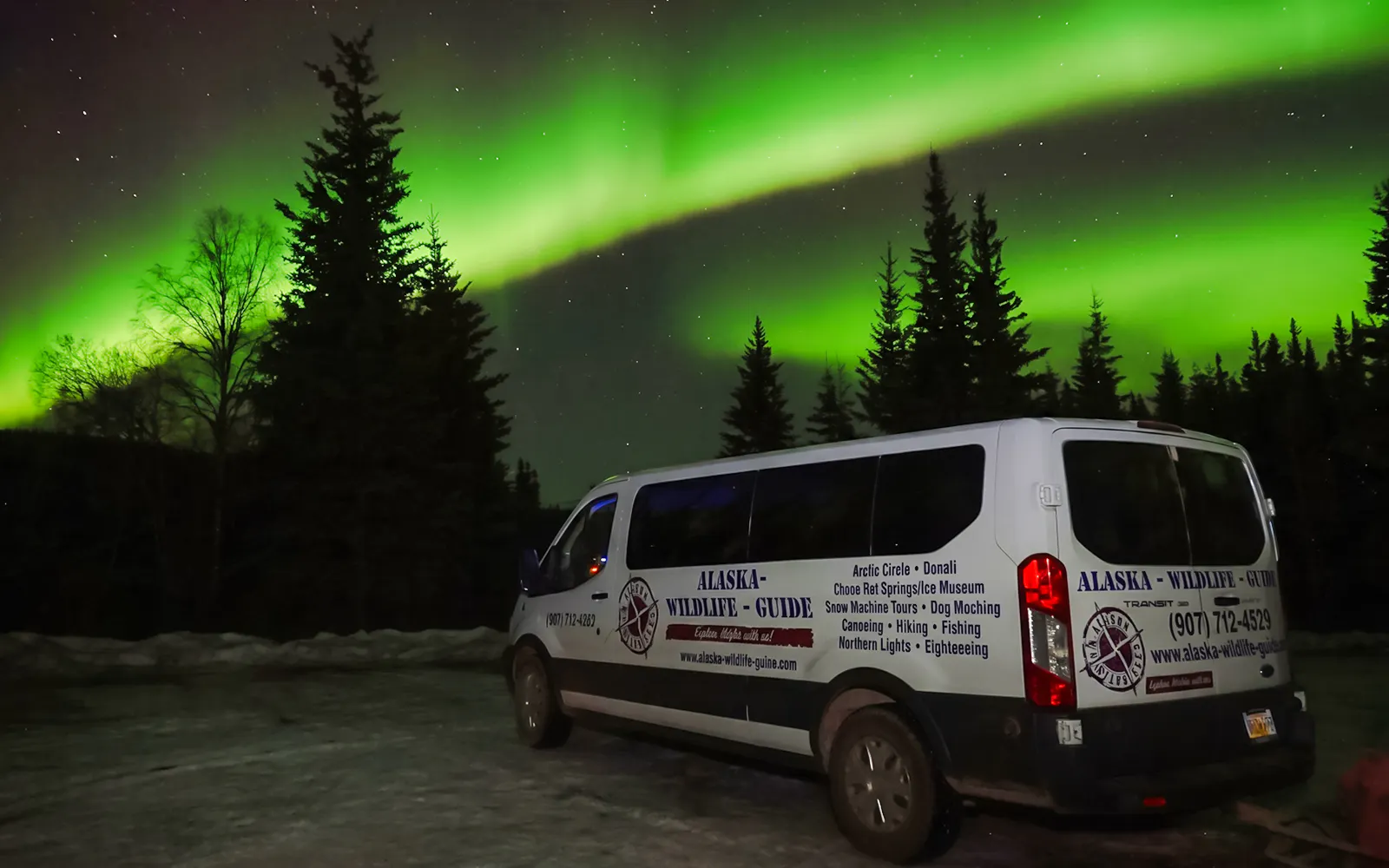 Tour van under Northern Lights in Alaska forest.