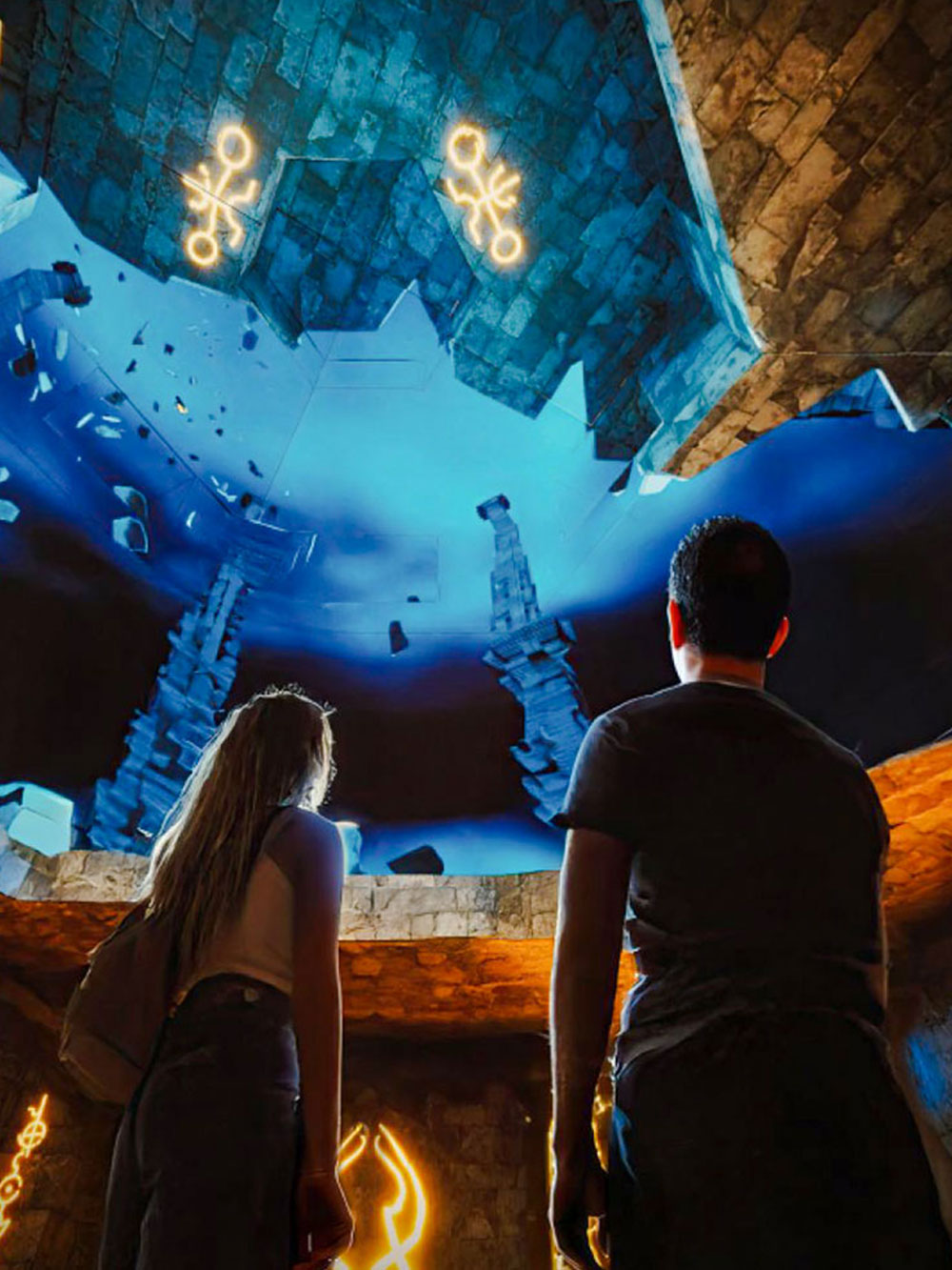 Visitors observing illuminated symbols and stone structures at The Lost World Aquarium.
