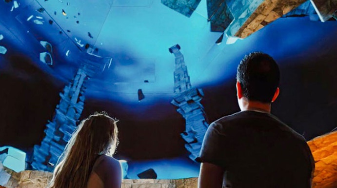 Visitors observing illuminated symbols and stone structures at The Lost World Aquarium.