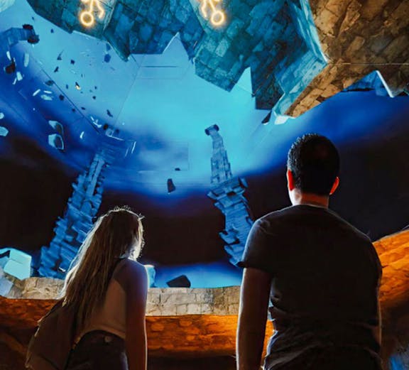 Visitors observing illuminated symbols and stone structures at The Lost World Aquarium.