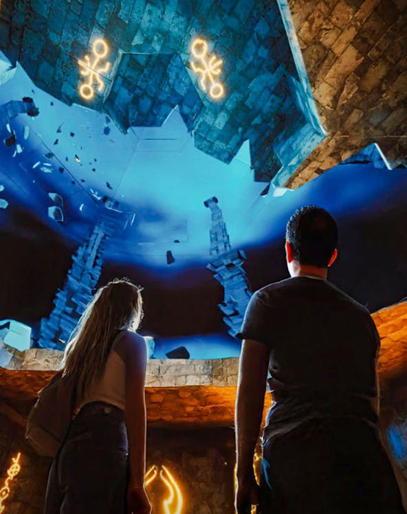 Visitors observing illuminated symbols and stone structures at The Lost World Aquarium.