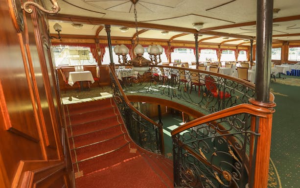 Elegant dining area on a Budapest evening dinner cruise with ornate staircase and tables.