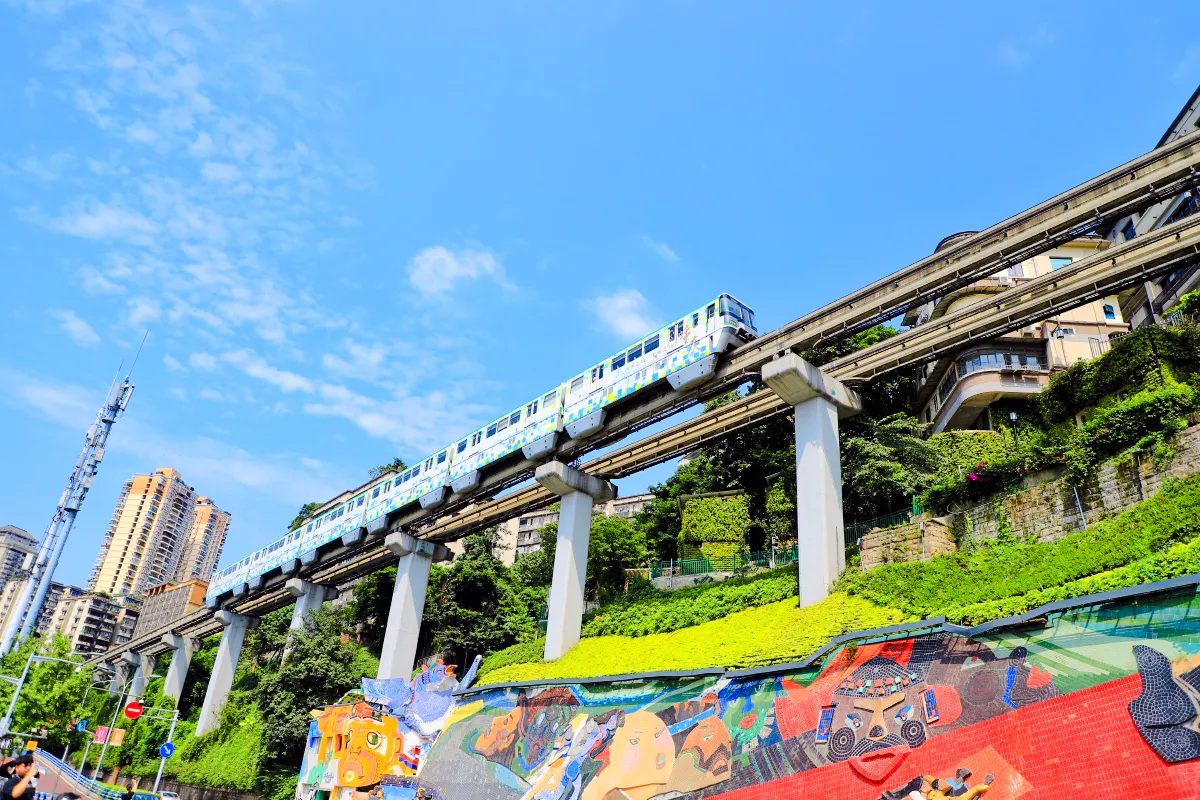 Chongqing monorail passing above colorful mural and city buildings.
