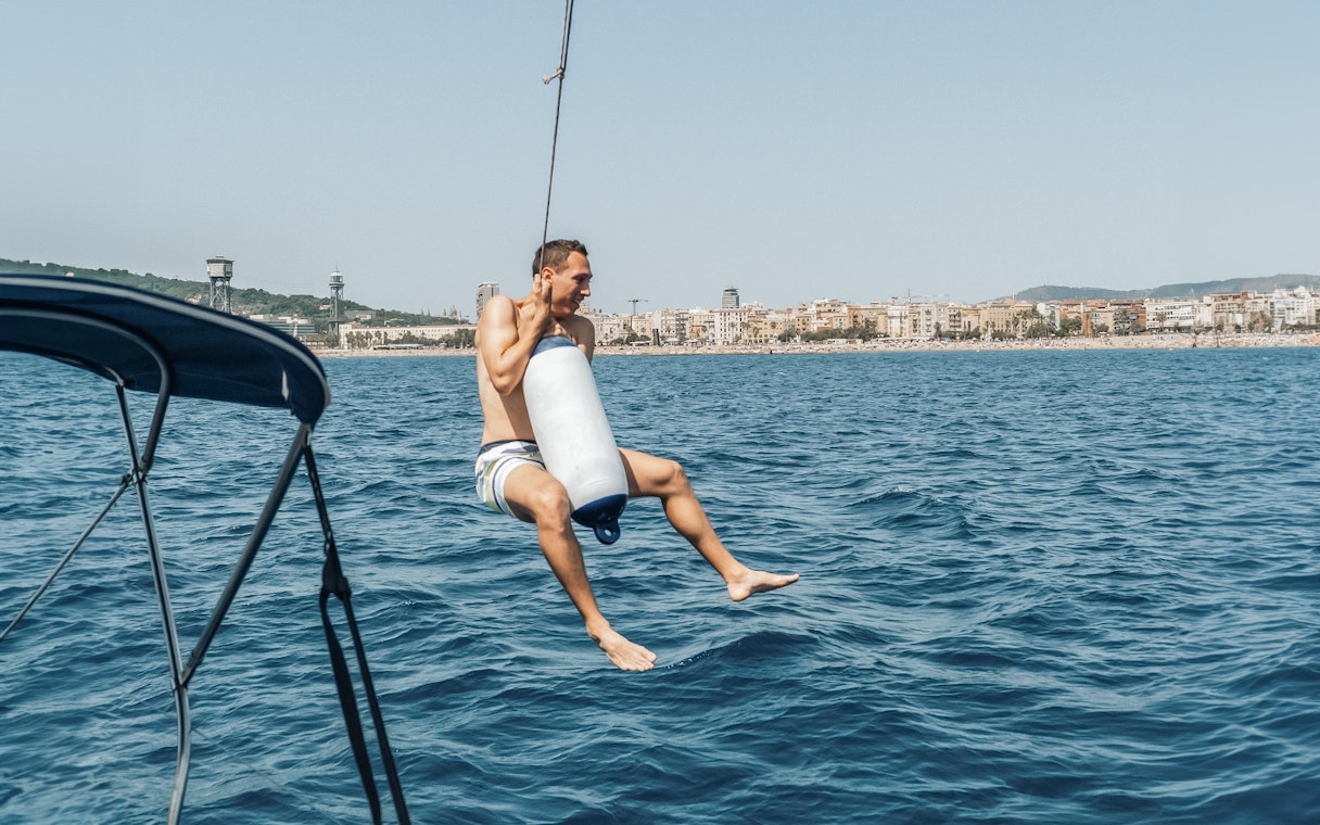 Sailor swinging over the sea near Barcelona on a Magic Sailing Experience.