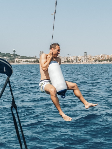 Sailor swinging over the sea near Barcelona on a Magic Sailing Experience.