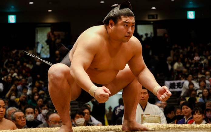 Sumo wrestler crouching, focused on opponent in a crowded arena, Japan.