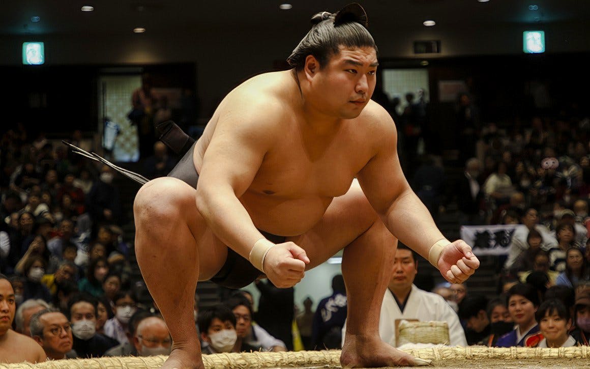 Sumo wrestler crouching, focused on opponent in a crowded arena, Japan.