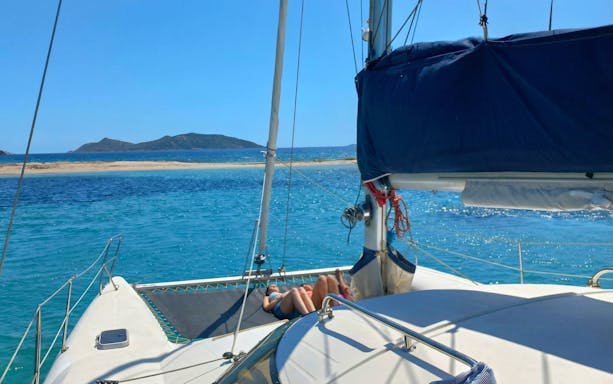 Catamaran sailing near Tavolara Island with passengers relaxing on deck.