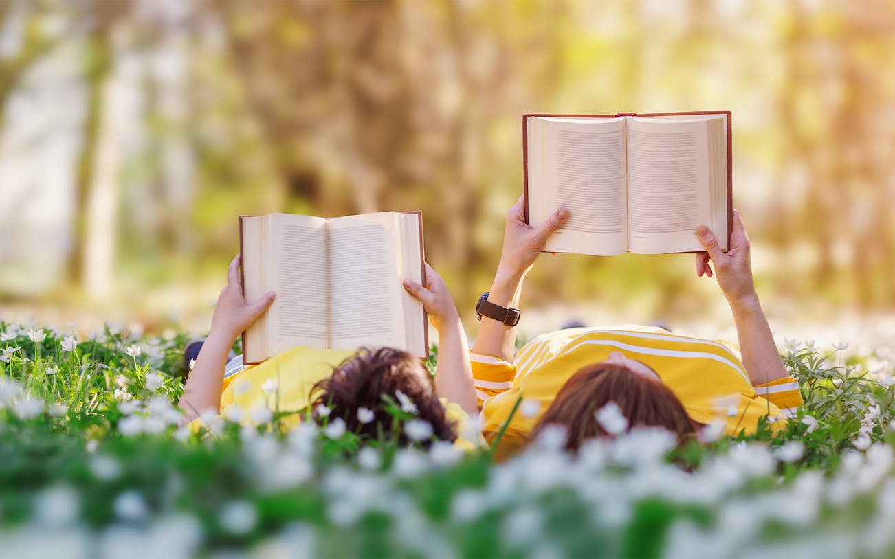 Mother and son reading books while lying in a park surrounded by flowers.