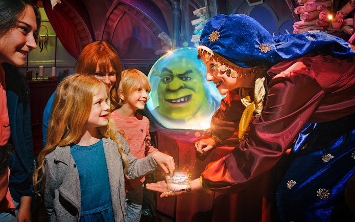 Visitors interacting with a character at Shrek's Adventure London, with Shrek in a crystal ball.