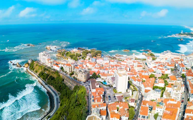 Aerial view of coastal town in Basque Country with ocean and red-roofed buildings.