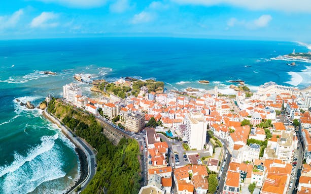 Aerial view of coastal town in Basque Country with ocean and red-roofed buildings.
