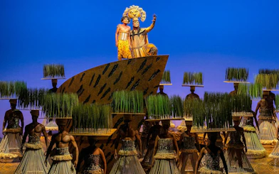 Performers in "The Lion King" musical on stage with vibrant costumes and set design.