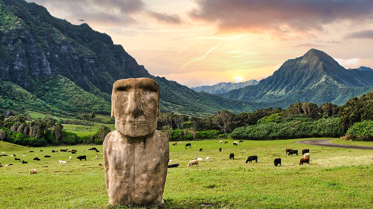 Moai statue with grazing cattle at Kualoa Ranch, Oahu, Hawaii, with lush mountains in the background.