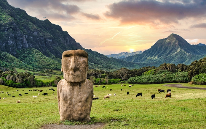 Moai statue with grazing cattle at Kualoa Ranch, Oahu, Hawaii, with lush mountains in the background.