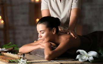 Woman receiving a back massage at Diora Spa with candles and flowers nearby.