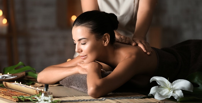 Woman receiving a back massage at Diora Spa with candles and flowers nearby.
