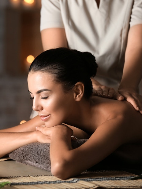 Woman receiving a back massage at Diora Spa with candles and flowers nearby.