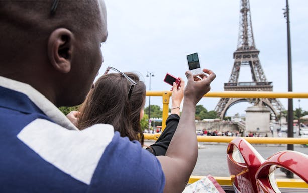 Passengers taking photos of the Eiffel Tower from a guided bus tour in Paris.