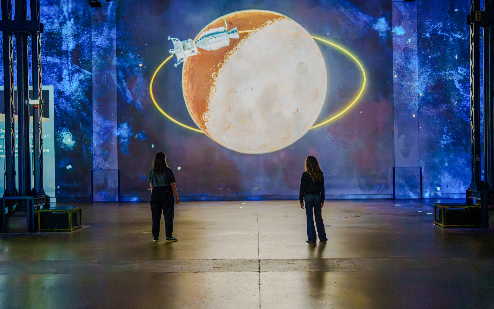 Visitors viewing a moon and spacecraft projection at The Moonwalkers Exhibition, Atelier des Lumières.