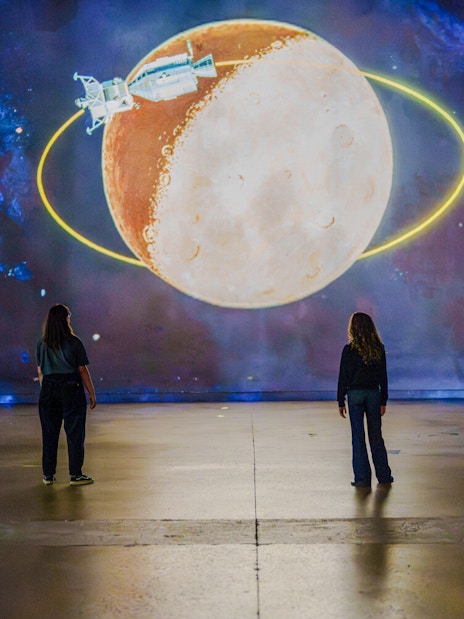 Visitors viewing a moon and spacecraft projection at The Moonwalkers Exhibition, Atelier des Lumières.