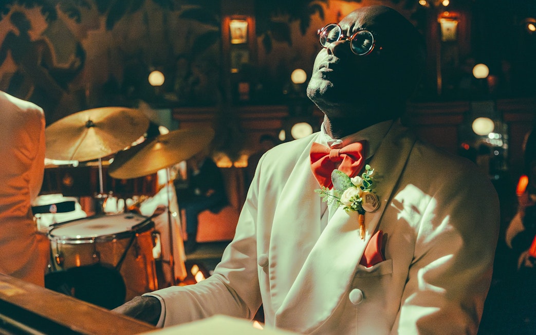 Musician in white suit performing at 58th Street venue with drum set in background.