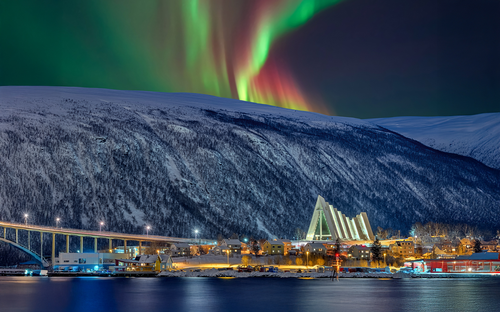 Arctic Cathedral illuminated at night with Northern Lights in Tromsø sky.