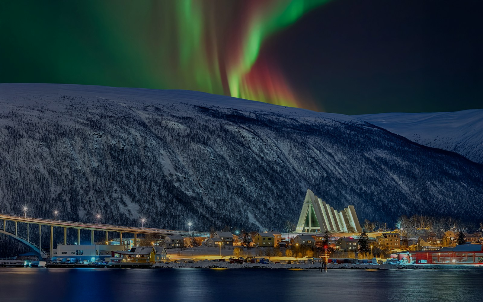 Arctic Cathedral illuminated at night with Northern Lights in Tromsø sky.