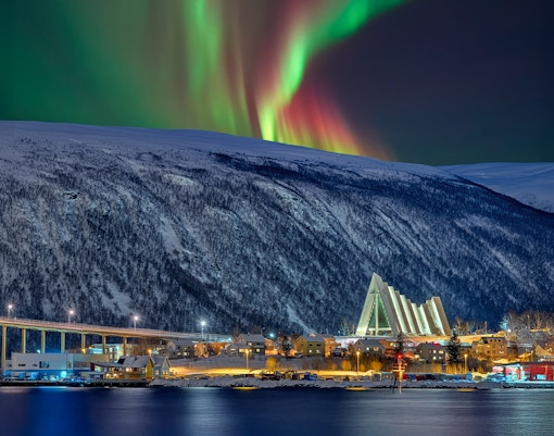 Arctic Cathedral illuminated at night with Northern Lights in Tromsø sky.
