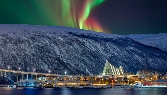 Arctic Cathedral illuminated at night with Northern Lights in Tromsø sky.