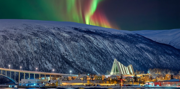 Arctic Cathedral illuminated at night with Northern Lights in Tromsø sky.