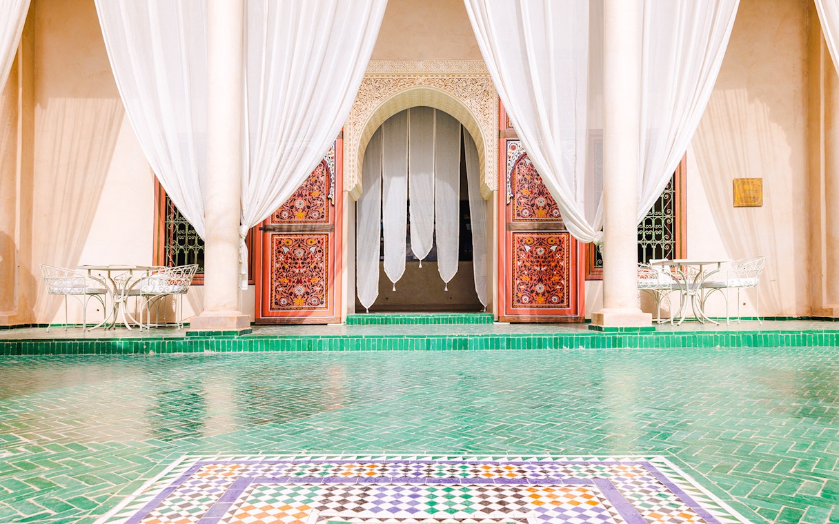 Ornate entrance with colorful tiles and white curtains at Jardin Secret, Marrakech, Morocco.