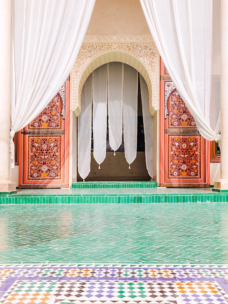 Ornate entrance with colorful tiles and white curtains at Jardin Secret, Marrakech, Morocco.