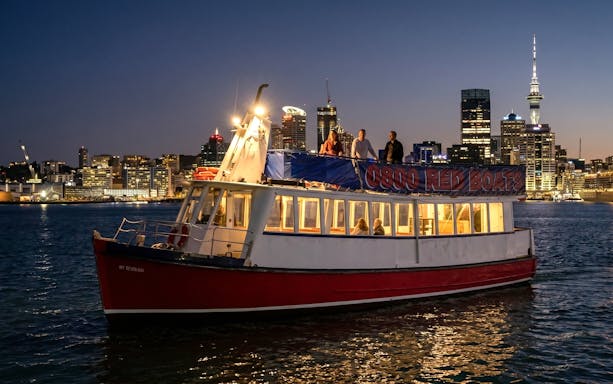 Auckland harbour cruise boat at night with city skyline in background.