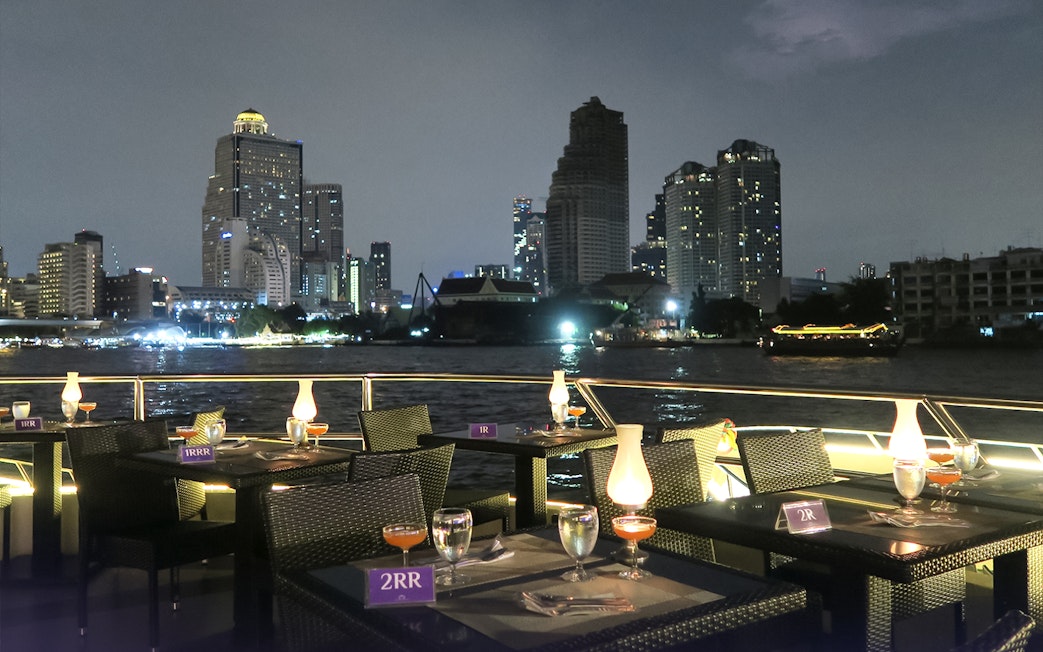 Dining setup on Chao Phraya Princess Cruise with Bangkok skyline at night.