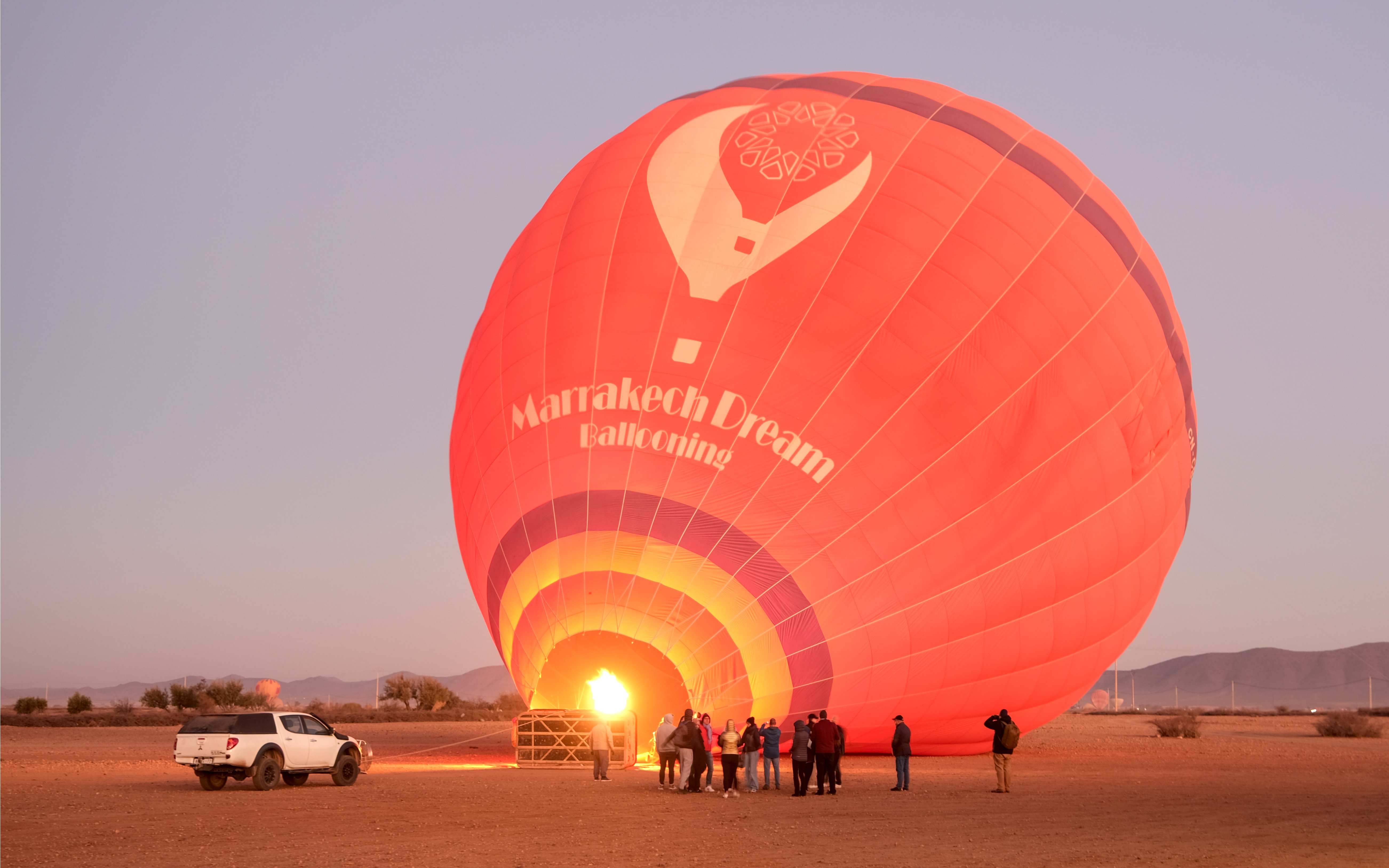 Hot air balloon inflating at sunrise in Marrakech, Morocco, with tourists observing nearby.