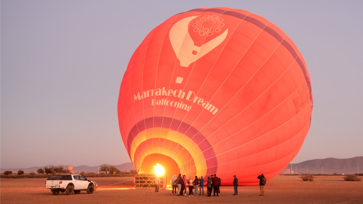 Hot air balloon inflating at sunrise in Marrakech, Morocco, with tourists observing nearby.