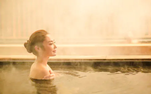 Person relaxing in a hot spring at Yunomori Onsen & Spa Sukhumvit Soi 26, Bangkok.