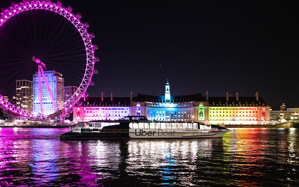 Uber Boat on Thames River at night with London Eye and illuminated buildings in background.