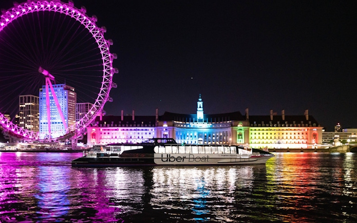Uber Boat on Thames River at night with London Eye and illuminated buildings in background.