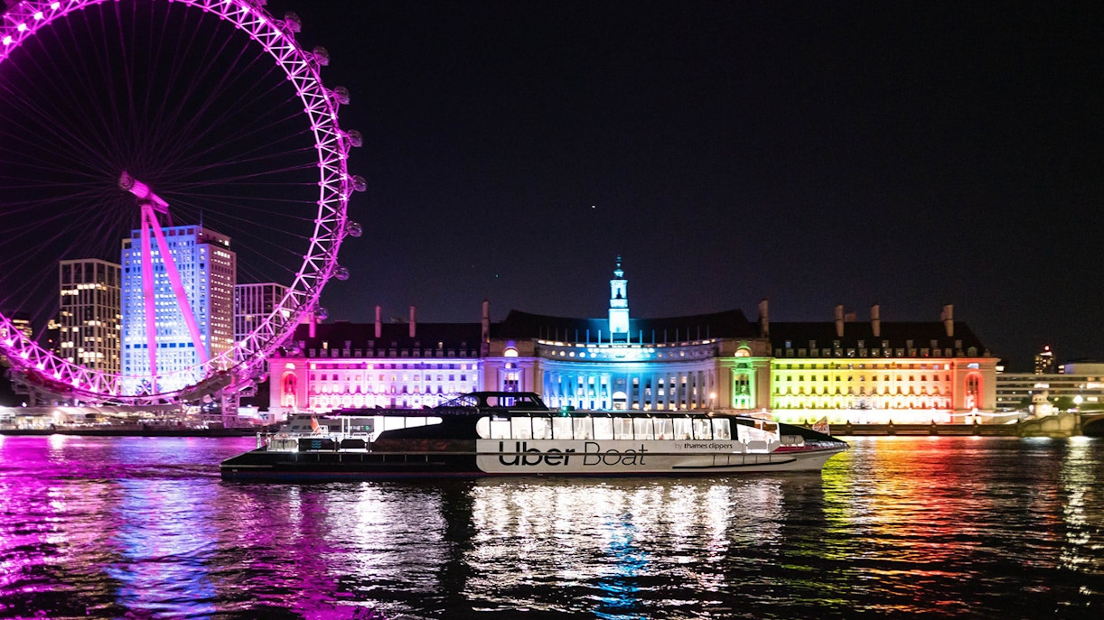 Uber Boat on Thames River at night with London Eye and illuminated buildings in background.
