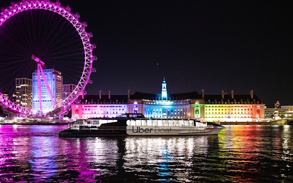 Uber Boat on Thames River at night with London Eye and illuminated buildings in background.