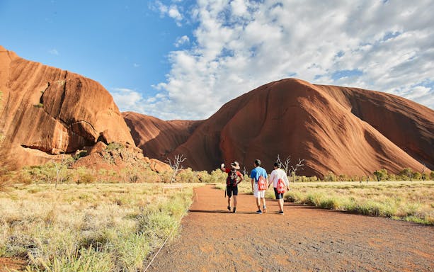 Guided group walking towards Uluru at sunrise, Australia.
